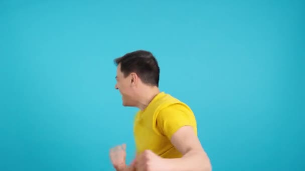 興奮し、幸せな男を祝うと踊りの青い背景を持つスタジオでのビデオ.モデルが表示され、下側からフレームから消えます. - 映像、動画