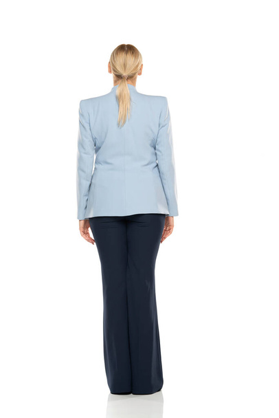 Middle aged senior woman  wearing blue jacket and black trousers on a white studio background. Rear, back view. - Foto, immagini
