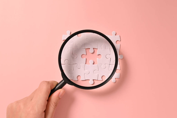 Hand holding magnifying glass with white square puzzle pieces grid of business background, Jigsaw on background, Mock up on background with copy space for text or symbols, Background with copy space - Photo, image
