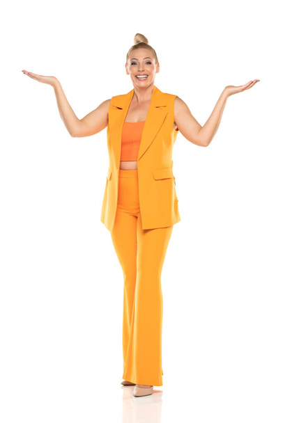 Middle aged advertising senior business woman in yellow sleeveless jacket and trousers posing on white studio background. Front view. - Foto, afbeelding