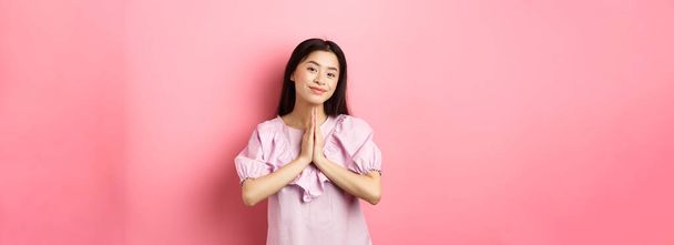 Aranyos ázsiai lány azt mondják köszönöm, mosolygós és boldognak néz ki, mutatja namaste gesztus a hála, álló ruha ellen rózsaszín háttér. - Fotó, kép
