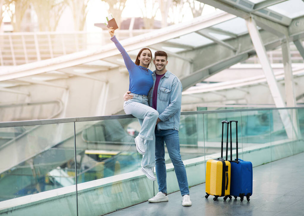Предложение проездных билетов. Счастливая романтическая пара туристов позирует с паспортами и посадочные талоны на автобусной станции или в аэропорту терминала, мужчина держит жену весело перед полетом. Полная длина - Фото, изображение