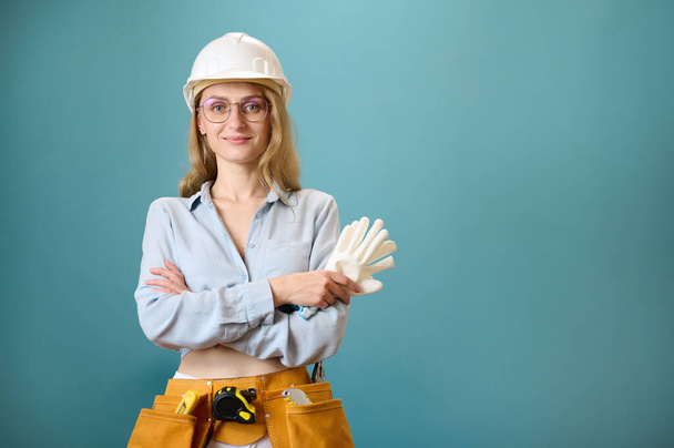 Portrait of young female worker with tool belt with crossed hands isolated on background. Pretty caucasian female with tools planning new project. Portrait in studio. Copy space. - Photo, Image