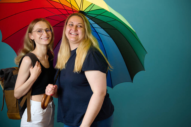 Two happy young lesbian girls hug under a colorful umbrella. Attractive carring female support, lesbian couple standing and hugging. - Photo, Image