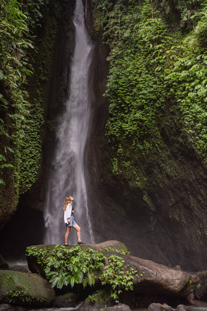 Travel lifestyle. Young traveler woman at waterfall in tropical forest. Leke Leke waterfall, Bali, Indonesia - Foto, imagen