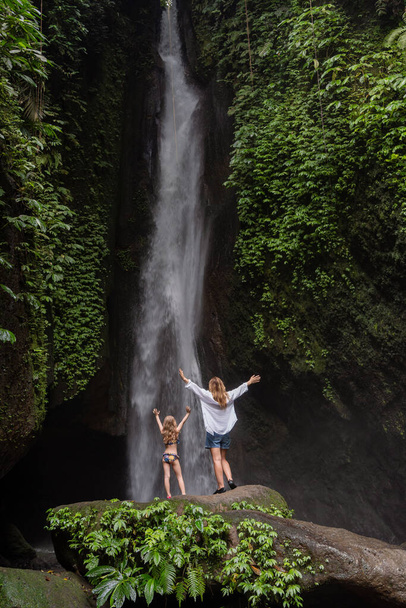 Family at a tropical waterfall. A woman and child at a beautiful waterfall. Vacation on a tropical island. Traveling couple at the waterfall. Family on vacation in Bali - Foto, imagen