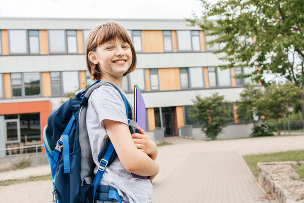 Egy boldog tinédzser lány portréja, hátizsákkal a hátán, az iskola előtt, tankönyvekkel a kezében. Vissza az iskolába, a tanév kezdete - Fotó, kép