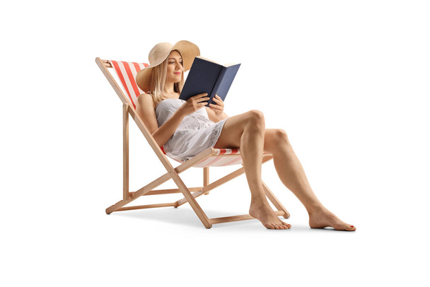 Beautiful young woman in a white dress sitting on a beach chair and reading a book isolated on white background - Photo, image
