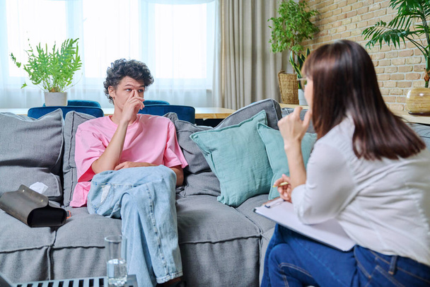 Young male having mental therapy in psychologists office. Guy college student talking to therapist, female counselor listening talking making clipboard notes. Support psychology psychotherapy concept - Photo, image