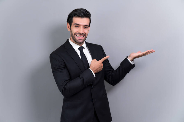 Уверенный бизнесмен в формальном костюме показывает пальцем и рукой жест, указывающий на продвижение или рекламу на пустом пространстве с возбужденным выражением лица на изолированном фоне. Пылкий - Фото, изображение