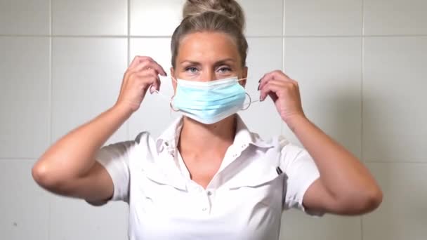 Naislääkäri laittaa kasvot suojaava steriili naamio lääketieteellisessä toimistossa klinikalla. Turvallista lääkettä. Terveydenhuollon työntekijä - Materiaali, video