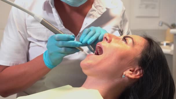 Zubař vyšetřující ústní dutiny úst pacienta v zubním křesle se zrcadlem a nářadím v ordinaci. Hygiena a zdraví ústní zuby - Záběry, video