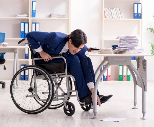Молодой работник в инвалидной коляске работает в офисе
 - Фото, изображение