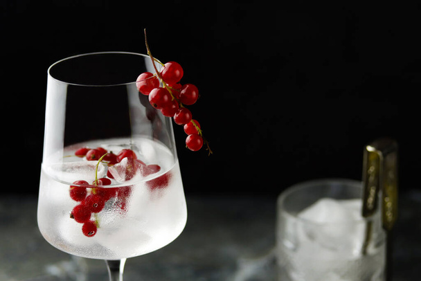 Extreme close up of wine glass with iced red currant water. Fresh ice cold fruit cocktail in glass, refreshing summer red currant berry drink with on dark background, front view. Red currant drink - Φωτογραφία, εικόνα
