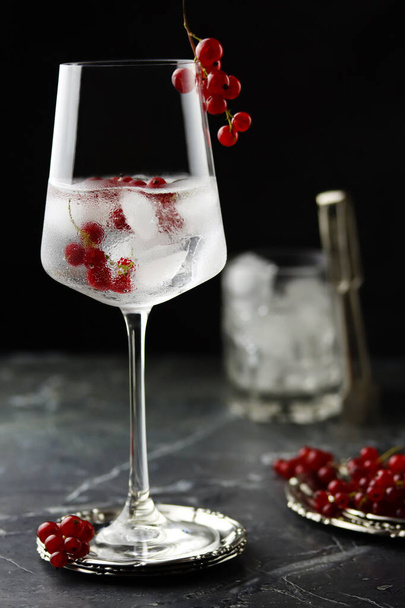 Iced red currant drink in wine glass. Fresh ice cold fruit cocktail in glass, refreshing summer red currant berry drink with on stone concrete background, front view, copy space. Red currant water - Photo, Image