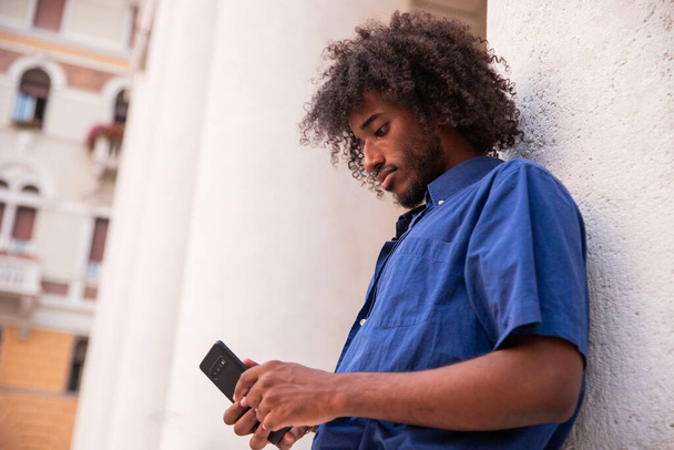 Un garçon africain se concentre sur l'utilisation de son smartphone, portrait extérieur - Photo, image