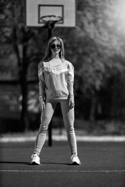 athletic blonde girl stands on the basketball court in a gray tracksuit black and white - Фото, зображення