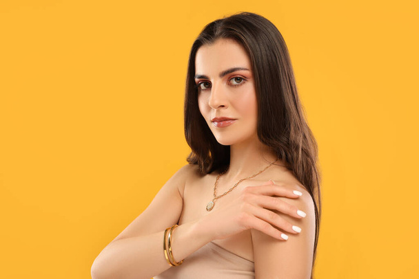 Beautiful woman with elegant jewelry on orange background, space for text - Foto, afbeelding