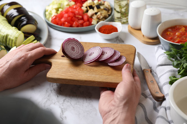 Cooking delicious ratatouille. Woman holding board with cut fresh onion at white marble table, closeup - Foto, afbeelding