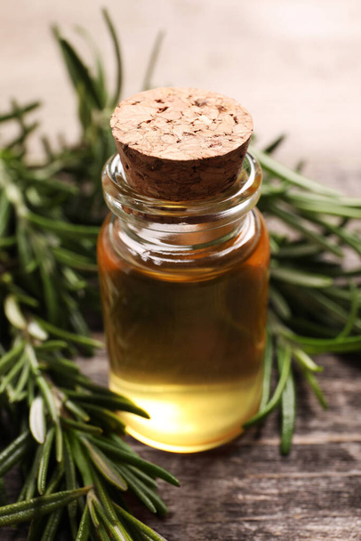 Bottle of essential oil and fresh rosemary on wooden table, closeup - Foto, imagen
