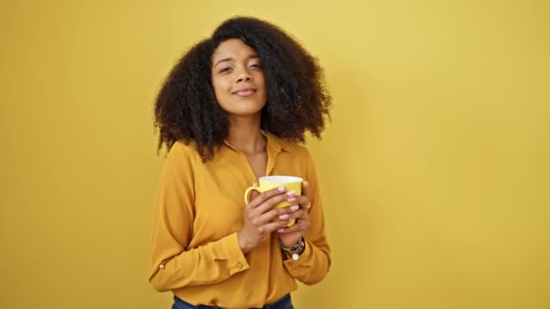 隔離された黄色の背景の上に立っているコーヒーを飲むアフリカ系アメリカ人女性 - 映像、動画