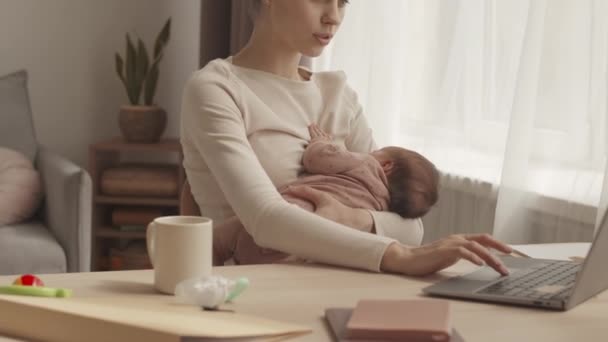 Waist up slowmo of young woman with infant baby daughter working on laptop from home, sitting at desk in cozy living room - Materiał filmowy, wideo