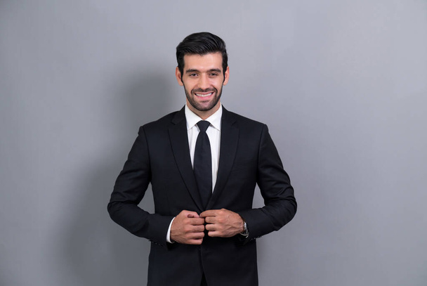 Stylish businessman in black suit posing confidently on isolated background, with a happy and optimistic smile as success and professionalism for businessman. Fervent - Foto, afbeelding