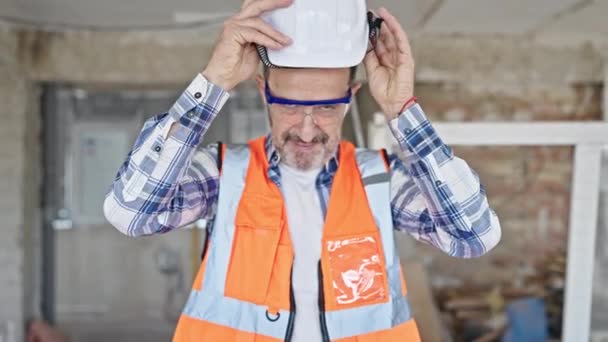 Constructor hombre de mediana edad sonriendo confiado usando hardhat en el sitio de construcción - Metraje, vídeo