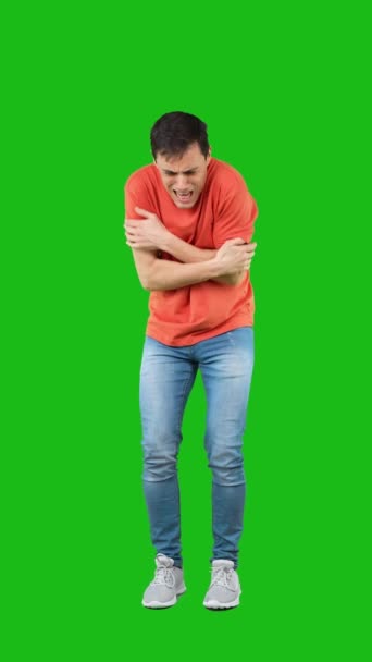 Full body of dissatisfied young male with dark hair in orange t shirt and jeans rubbing arms and looking at camera. Chroma key - Felvétel, videó