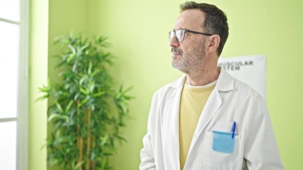 Mann mittleren Alters steht mit ernstem Gesichtsausdruck mit Stethoskop in Klinik - Filmmaterial, Video
