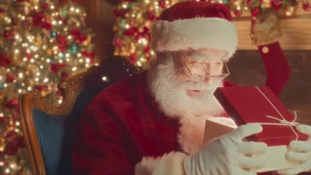 Waist up slowmo portrait of surprised bearded Santa opening beautiful Christmas present box and looking at camera - Imágenes, Vídeo
