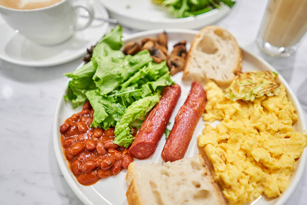 Einfaches amerikanisches Frühstück mit Würstchen, Rührei, Bohnen, Pilzen und Tomaten. Dieses Gericht ist voller Nährstoffe, die Sie brauchten. Hochwertiges Foto - Foto, Bild