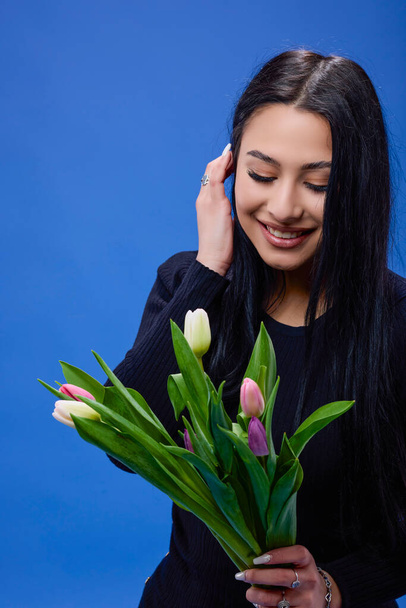 A beautiful young woman with tulips in her hand posing in the studio on a blue background - Foto, imagen