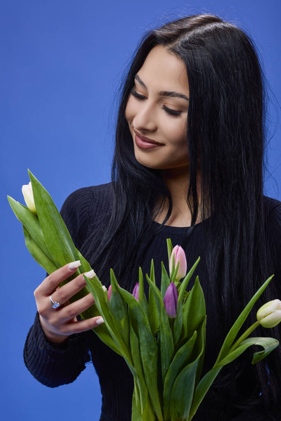 A beautiful young woman with tulips in her hand posing in the studio on a blue background - Foto, imagen