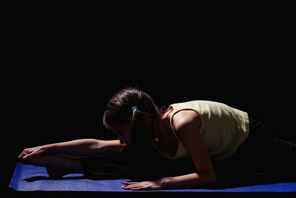 Portrait de jeune fille sportive faisant des exercices d'étirement de forme physique sur fond sombre.  - Photo, image