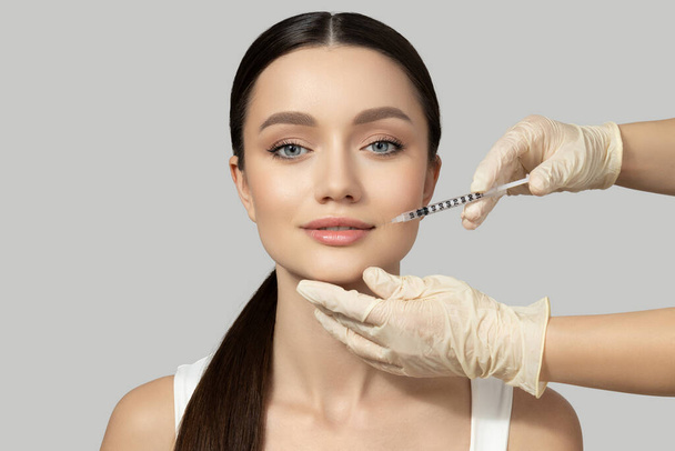 A beautiful girl makes an injection of botox, on a gray background - Photo, image