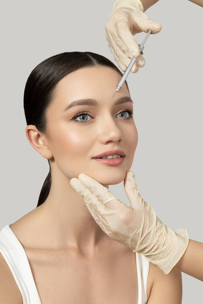 A beautiful girl makes an injection of botox, on a gray background - Fotoğraf, Görsel