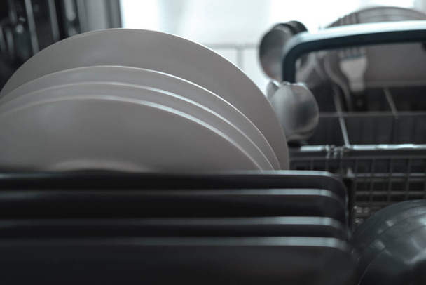 Полная посудомоечная машина с белыми и черными серыми тарелками, ежедневная рутина дома - Фото, изображение