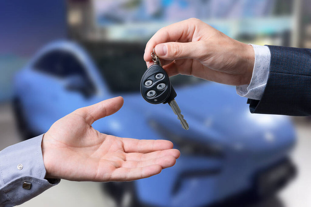 Auto business, car sale, transportation, people and ownership concept - close up of car salesman giving key to new owner or customer over auto show background - Photo, Image