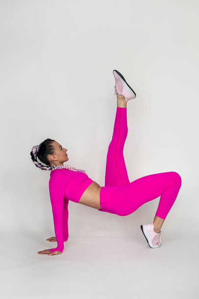 Sporty young woman doing stretching exercises in tracksuit isolated on pink background. Concept of healthy life and natural balance between body and mental development. Full length - Foto, Bild
