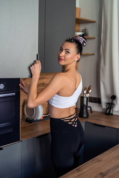 Portrait of an attractive woman holding a cup and a knife smiling in her kitchen. Beautiful sporty girl in sportswear enjoying coffee. training for health. concept of diet and healthy eating. - Fotoğraf, Görsel