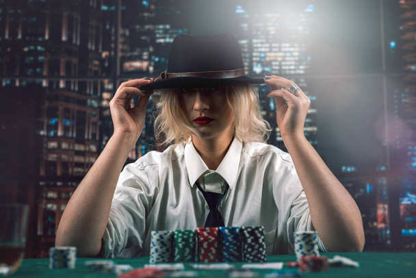 Hermosa chica repartidor en un sombrero en una camisa y corbata en la mesa de póquer. sigue el proceso. juego. engaño. maquinaciones - Foto, imagen