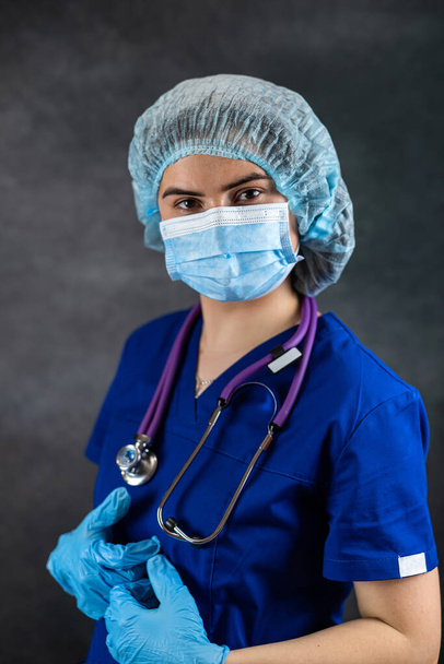 portrait of woman doctor or nurse wearing surgical mask and gloves with stethoscope isolated on dark. Woman hospital worker looking at camera, healthcare - Fotografie, Obrázek
