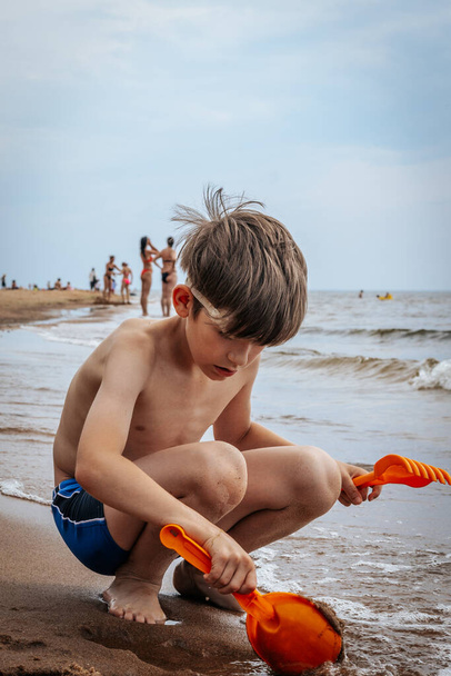 Мальчик играл с песком на берегу моря. Ребенок играл с морским песком на песчаном берегу моря. Мягкая селективная фокусировка - Фото, изображение
