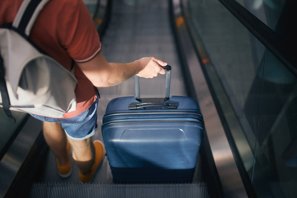 Reisende gehen durch das Flughafenterminal. Rückansicht eines Mannes mit Koffer und Rucksack, der auf einem Kühlschrank steht. Passagier ist reif für die Reise - Foto, Bild