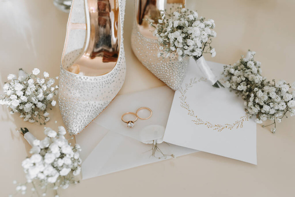 Wedding rings of the bride and groom with wedding bouquets of white flowers. Two beautiful gold wedding rings. Men's and women's rings with ornaments. Women's high-heeled shoes. place for text - 写真・画像