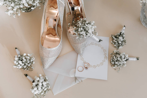 Jegygyűrűk a menyasszony és a vőlegény esküvői csokrok fehér virágok. Két gyönyörű arany jegygyűrű. Férfi- és női gyűrűk díszítéssel. Női magassarkú cipő. a szöveg helye - Fotó, kép