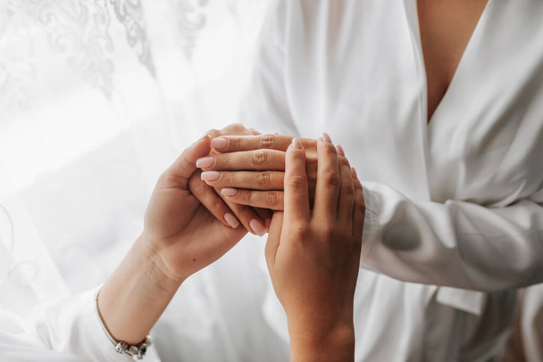 Girlfriends support the bride on her wedding day by holding hands in matching white robes - Foto, imagen