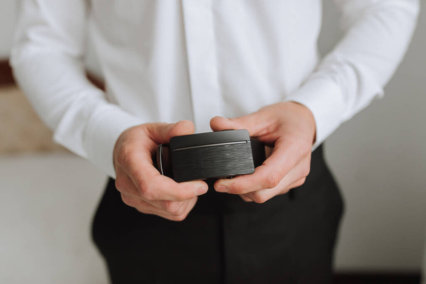 a young man in black pants holds his man's belt in his hands. The groom is preparing for the wedding ceremony. Detailed close-up photo of hands - Photo, Image