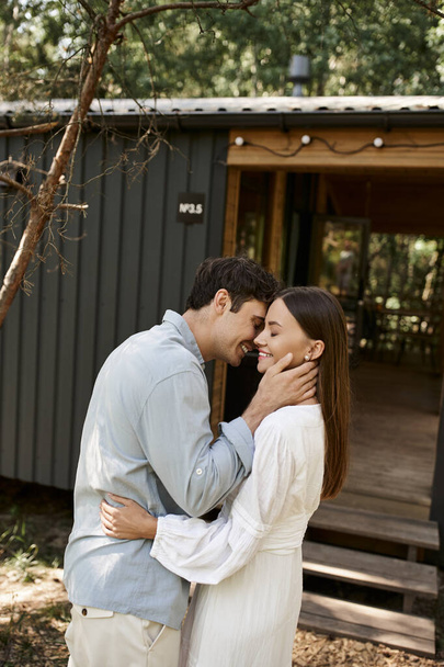 couple in love, handsome man hugging beautiful woman near vacation house, summer getaway, romance - Valokuva, kuva